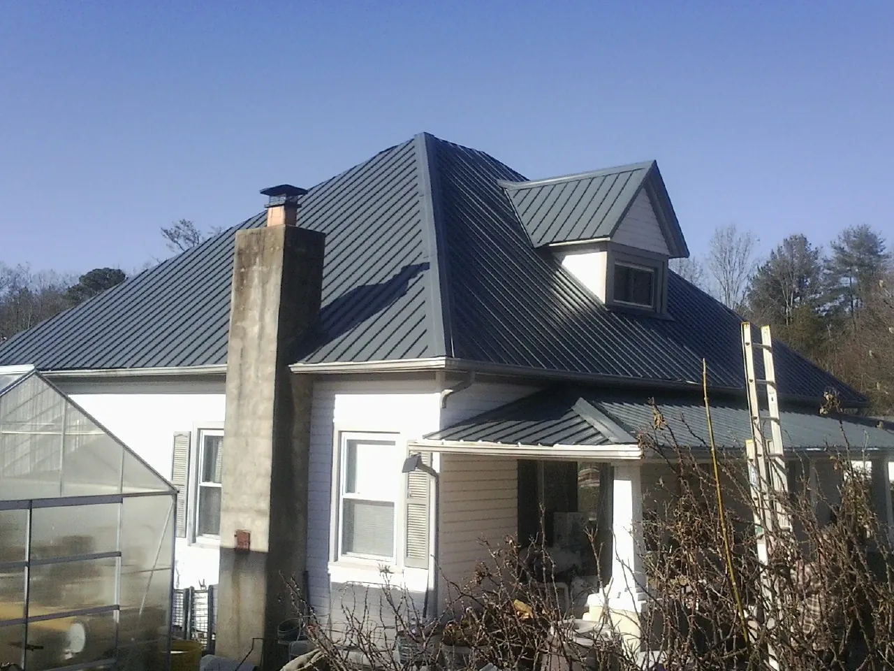 Dark blue standing seam metal roof on a white farmhouse with dormer — Slate & Tile Roof Repair by Roofing Brothers in Roy