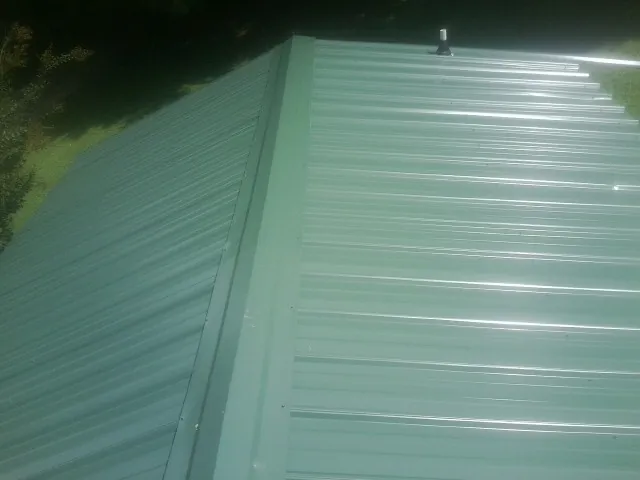 New green metal panels meeting at the ridge of a roof — Flat Roof Repair work by our crew in Roy
