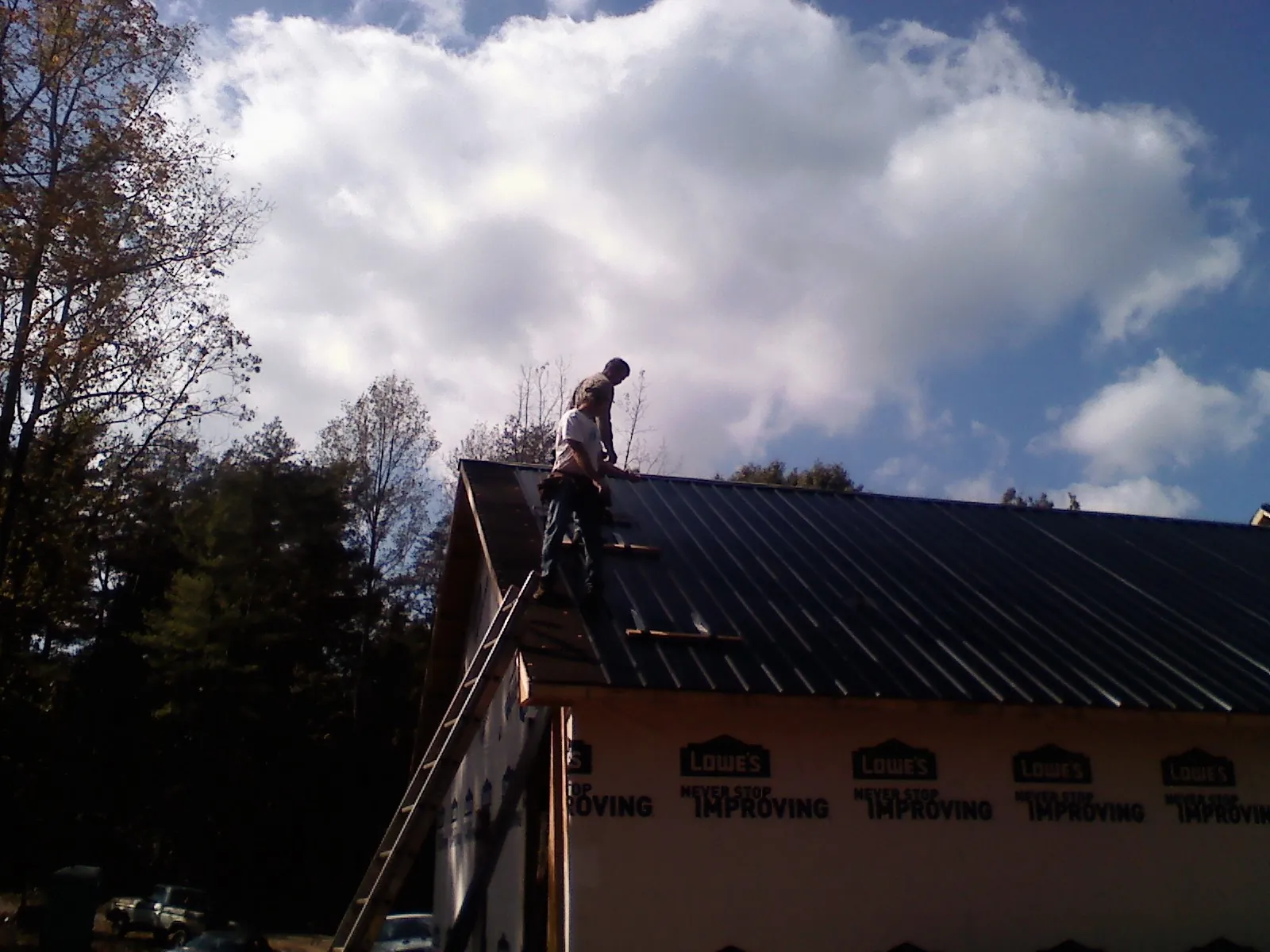Roofer fastening dark metal panels high against a cloudy sky, from a Roof Inspection job in Roy